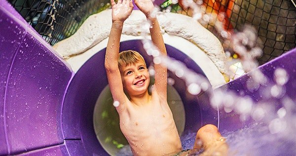 Overdekt waterpark Plopsaqua De Panne met glijbanen en zwembaden, omringd door groen.