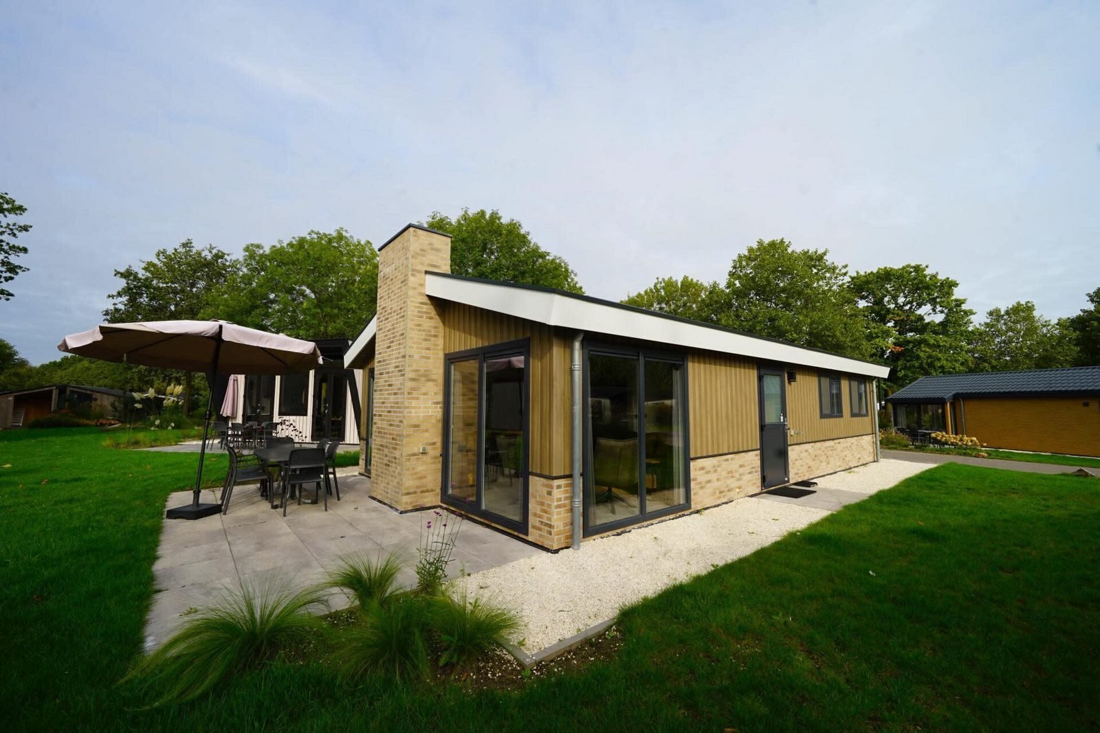 Afbeelding bij Luxe overnachten aan het water in Limburg en Noord-Holland: 4 bijzondere verblijven Luxe vakantiehuis aan het water met terras en uitzicht op een rustige plas, omgeven door groen.