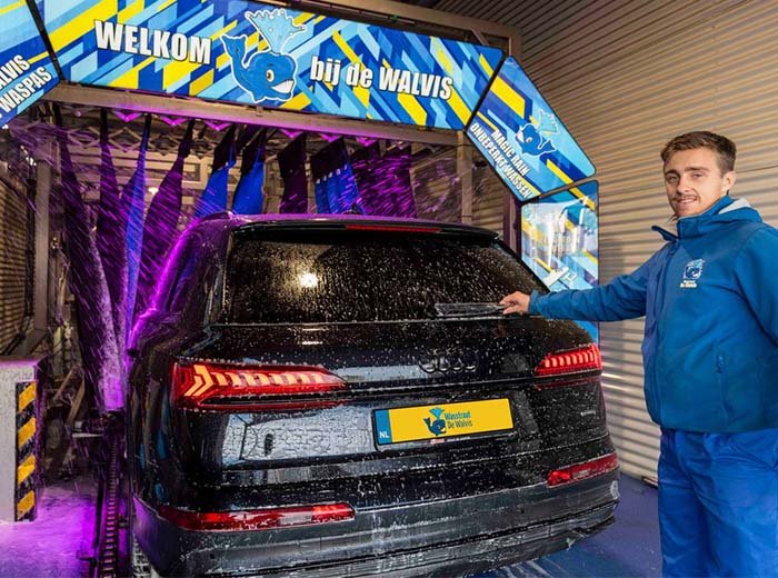 Een auto rijdt door de wasstraat bij Wasstraat de Walvis, met water en zeep op de voorruit.