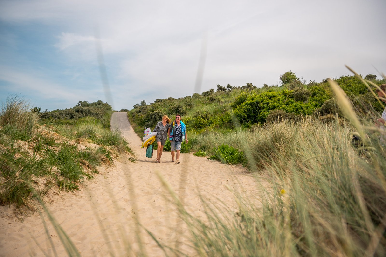 Een stel wandelt hand in hand over het zandstrand bij EuroParcs Schoneveld, met duinen op de achtergrond.