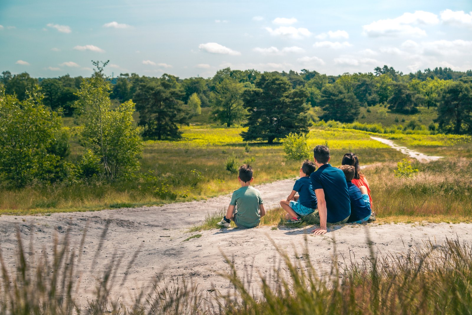 Gezin wandelt over de paarse heide van de Brunssummerheide in Zuid-Limburg, met glooiende heuvels op de achtergrond.
