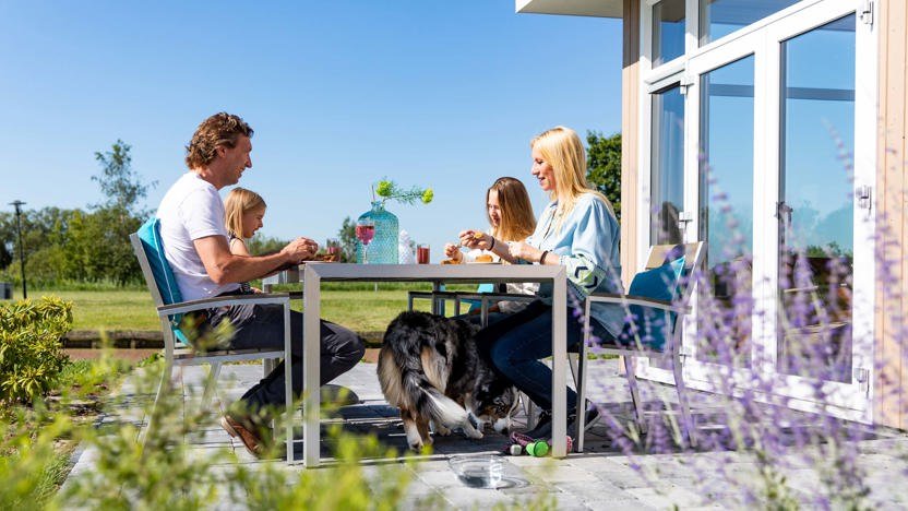 Afbeelding bij Parc de IJsselhoeve Vakantiegangers met hun hond op het terras van hun luxe vakantiehuisje bij Parc de IJsselhoeve in de Krimpenerwaard.