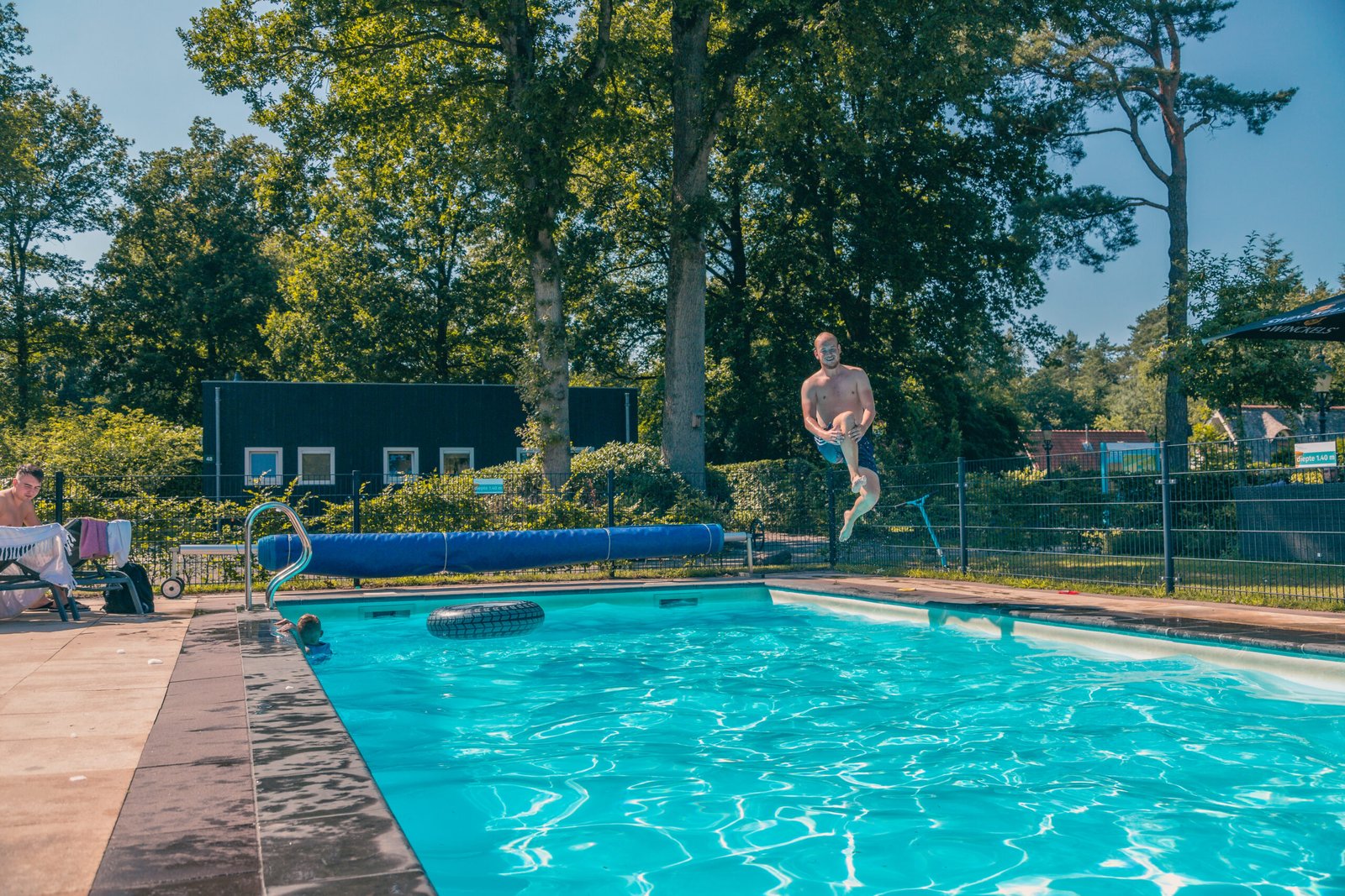 Een groot buitenzwembad met ligbedden en parasols bij EuroParcs Reestervallei, omringd door groen.